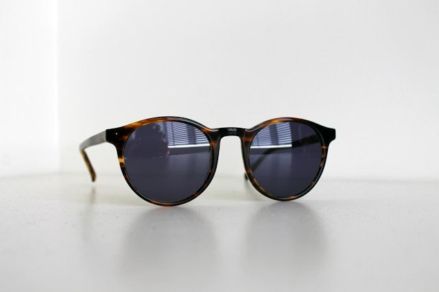 A pair of sunglasses with a tortoiseshell pattern frame, lying on a white surface.