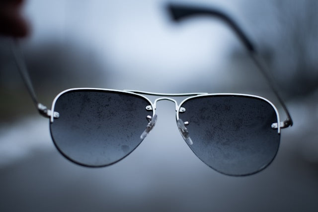 A pair of sunglasses with a silver metal frame, showing signs of tarnish or dirt on the lenses and frame.